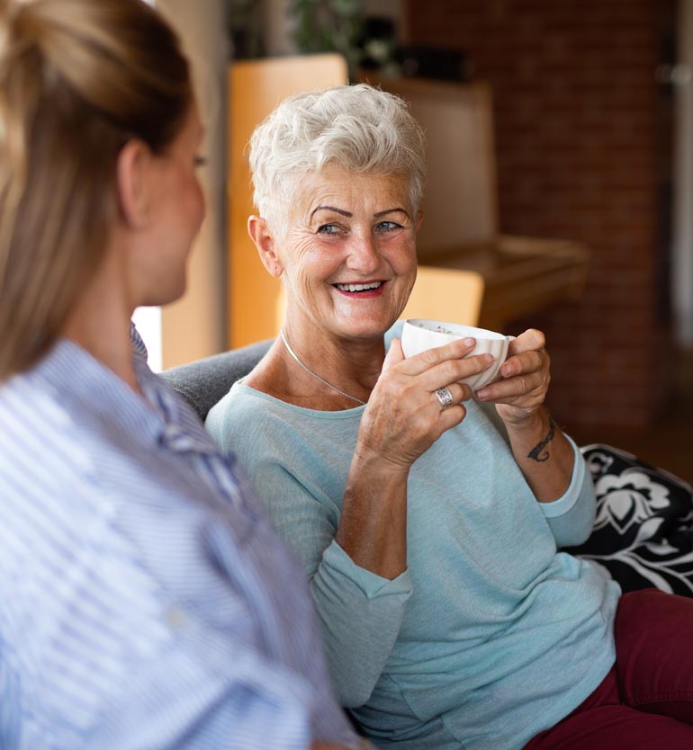 senior-with-team-member Smiling senior woman holding a cup, engaged in a pleasant conversation with a younger team member.