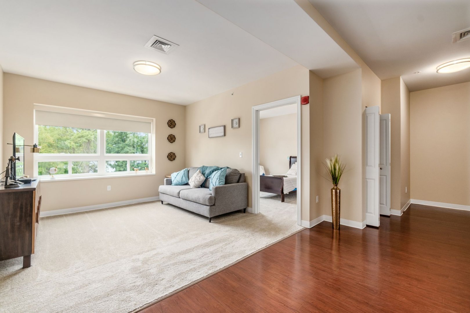 Bright living area with a couch, TV, and large windows connecting to a bedroom.