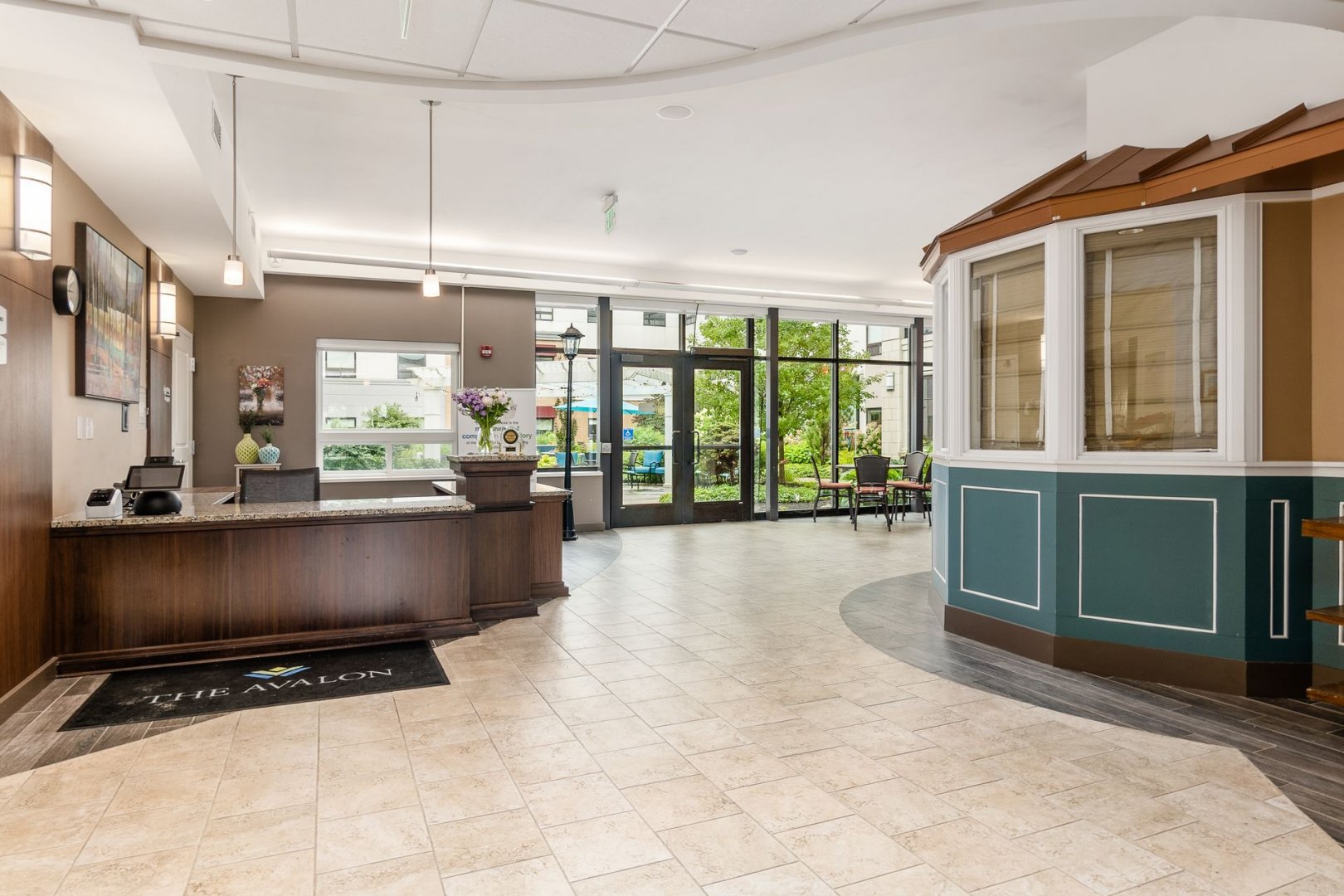 Bright lobby area with reception desk in a senior living community with large windows and seating area.