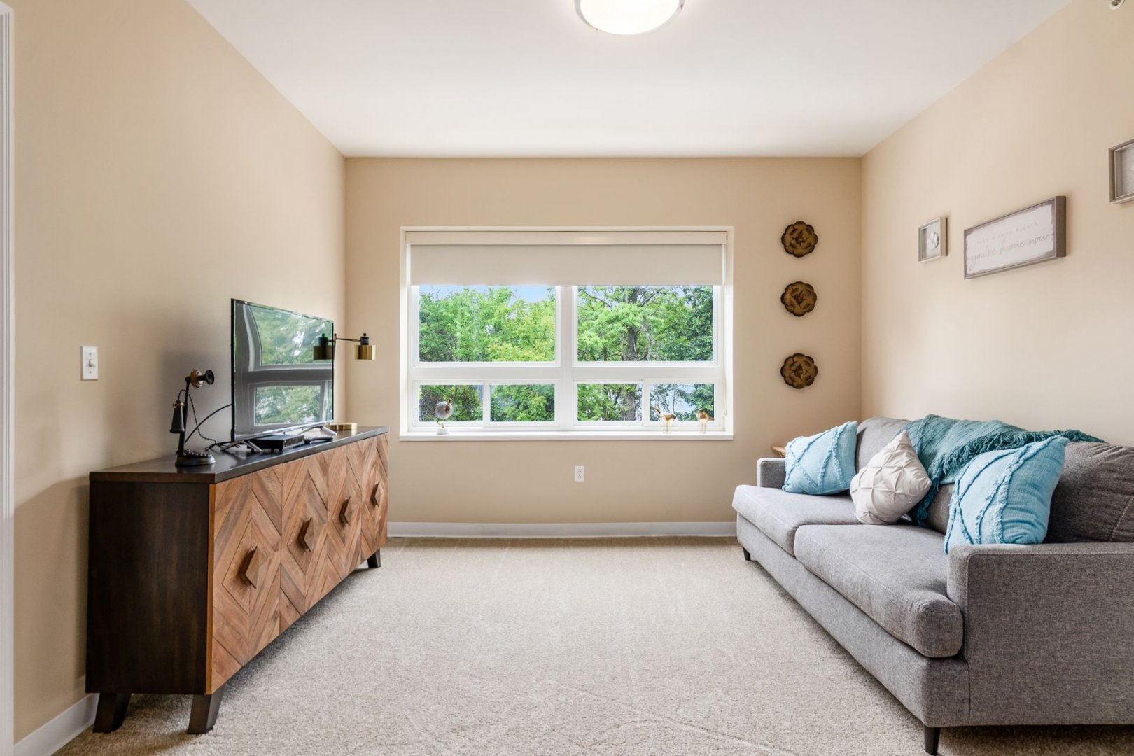 Bright living room in a senior living unit with a sofa, TV console, and large window.