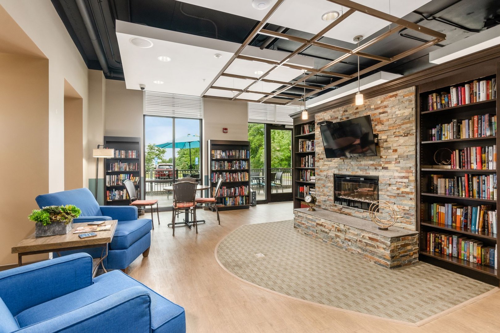 Comfortable library area with blue chairs, bookshelves, fireplace, and outdoor view.