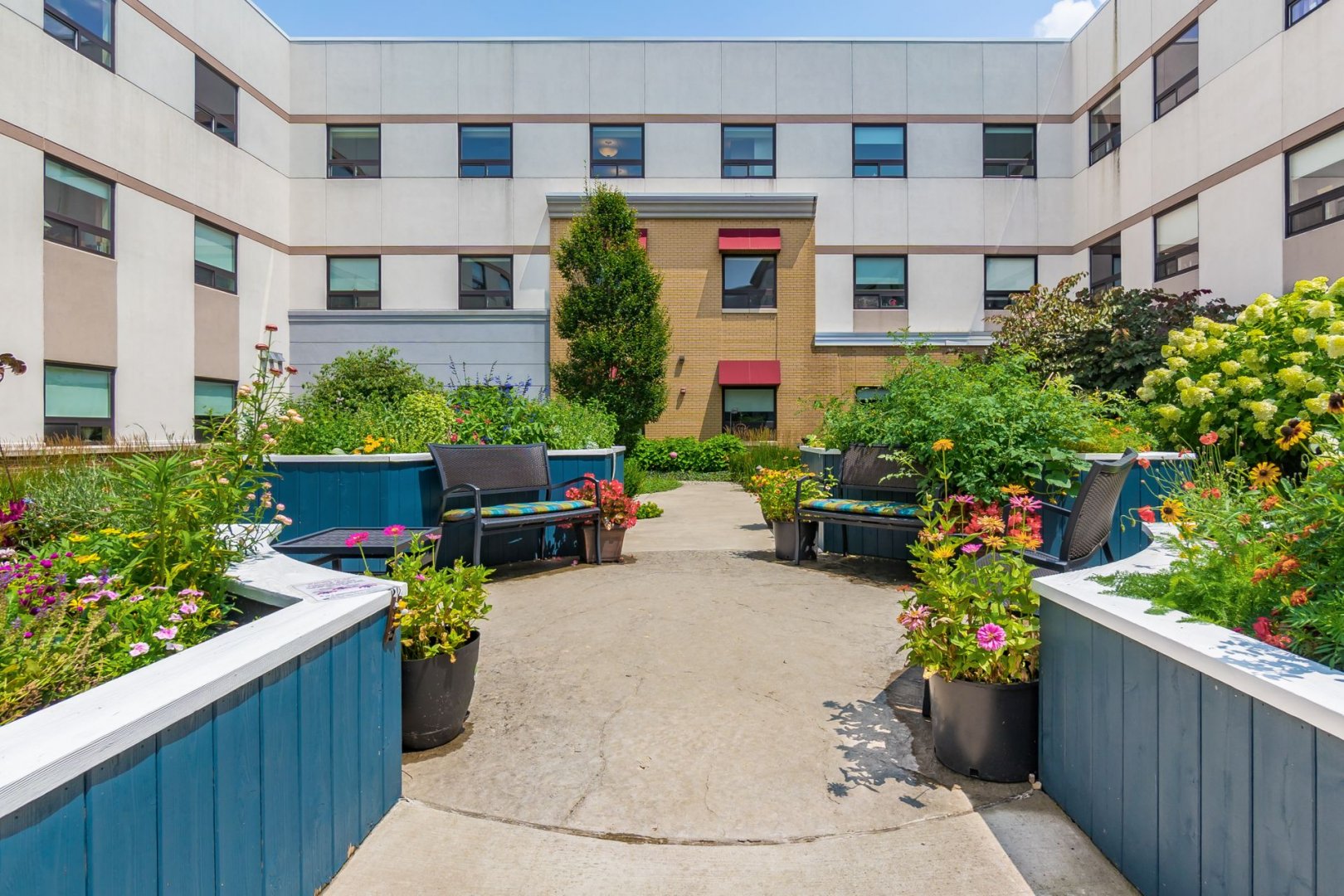 Courtyard with seating and vibrant flowers at a multi-story senior living community.