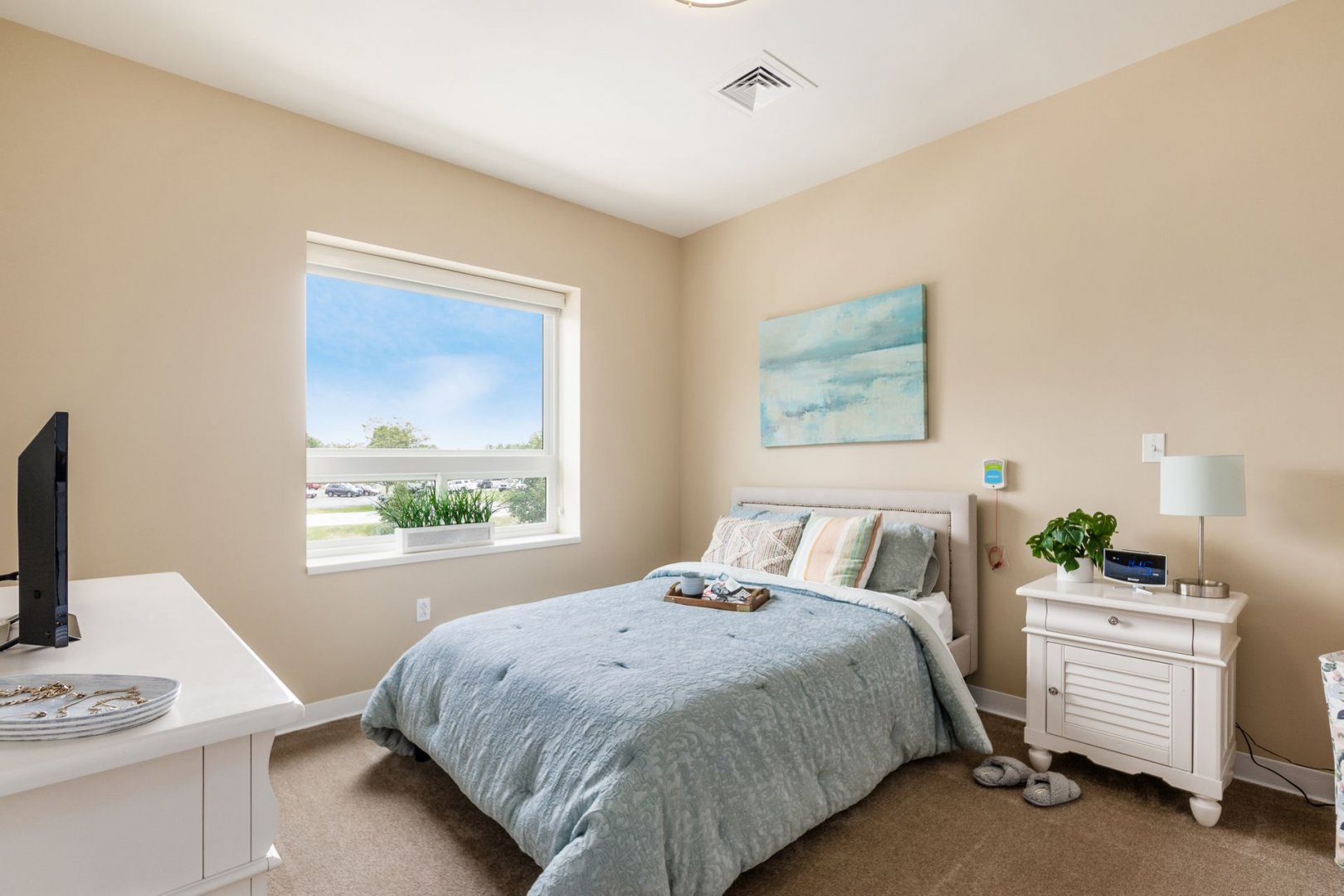 Bright, cozy bedroom with large window, light blue bedspread, and modern and elegant decor.