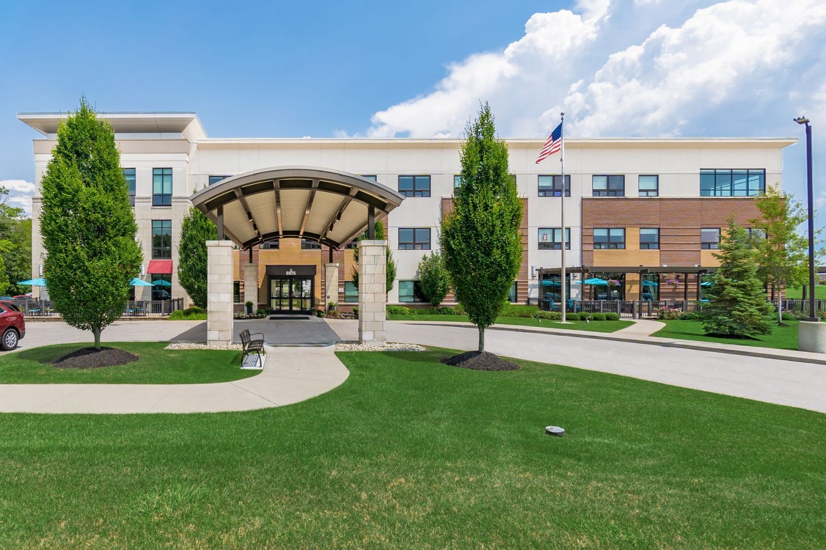 Front exterior view of a modern three-story senior living community with lush green landscaping.