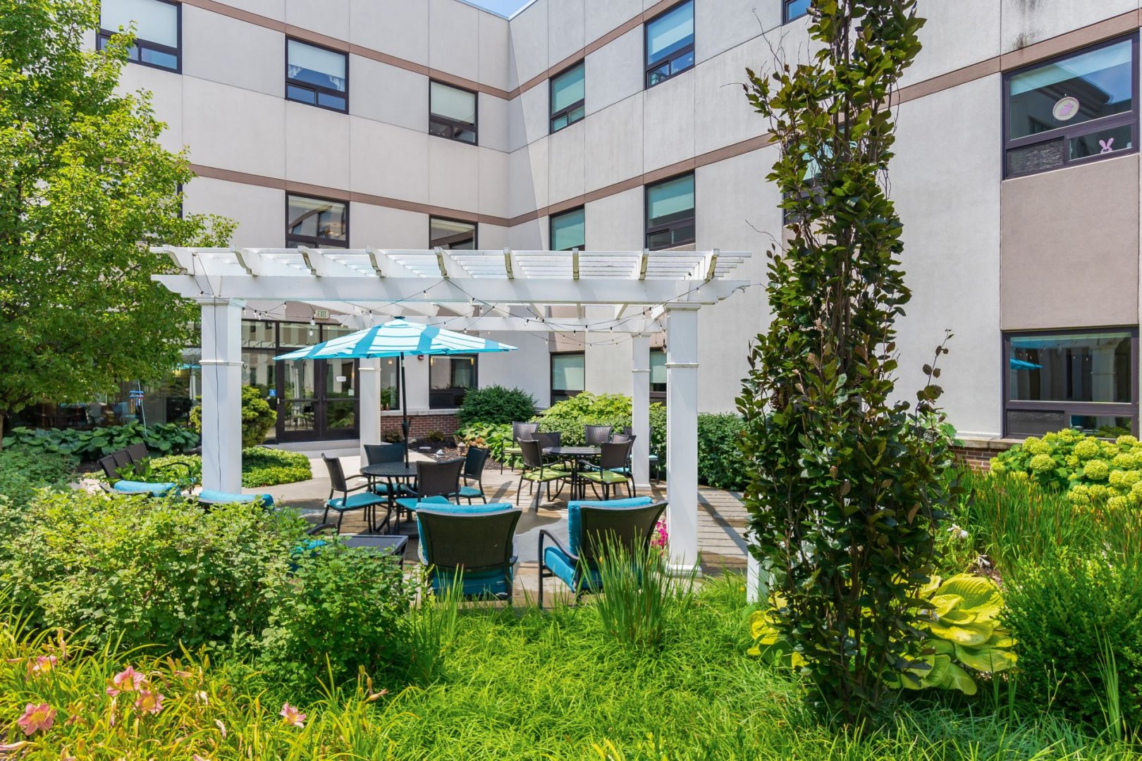 Outdoor seating area with umbrella tables and green surroundings at a residential living facility.