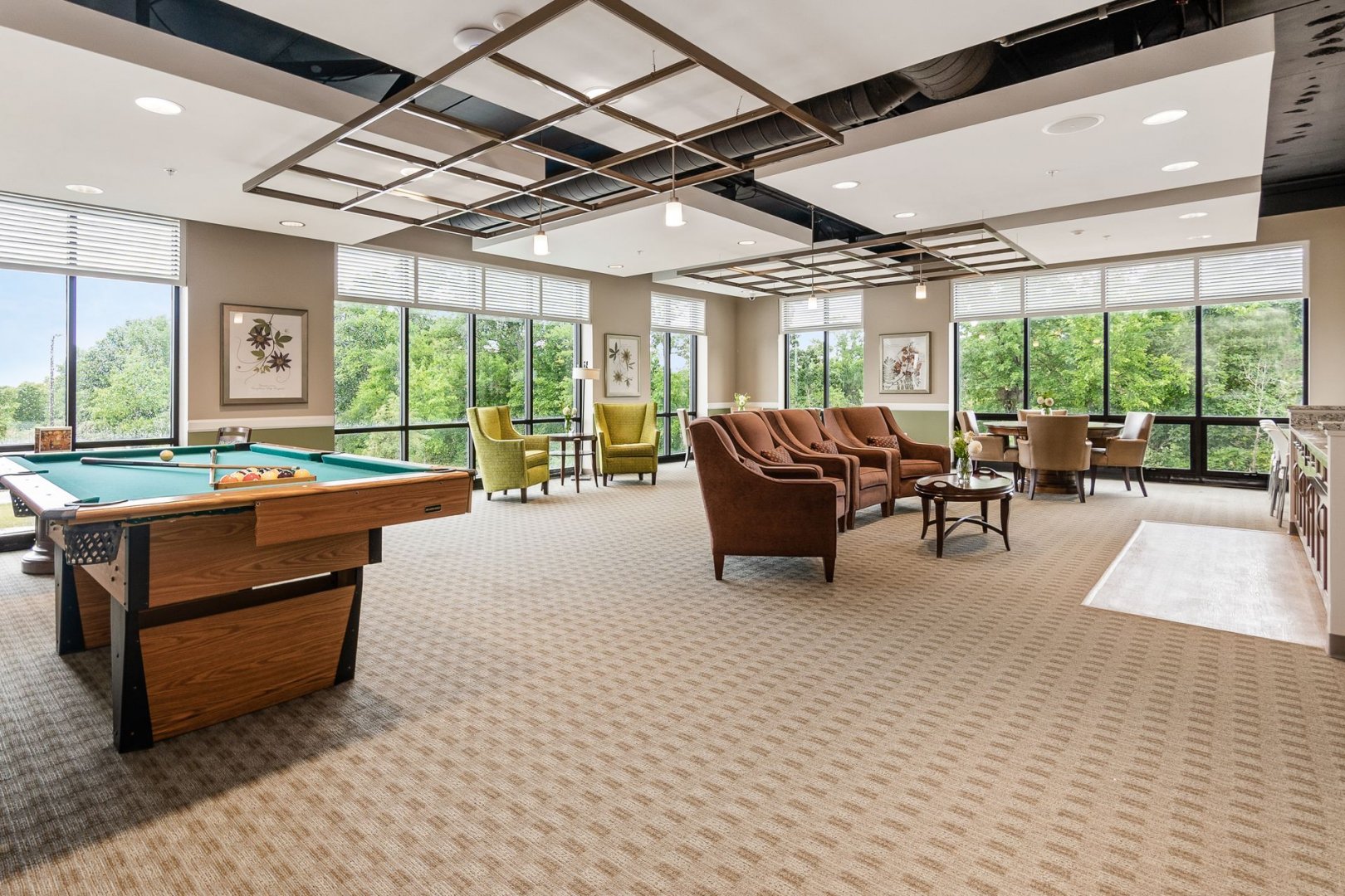 Common area of a senior living community with seating, pool table, and large windows.